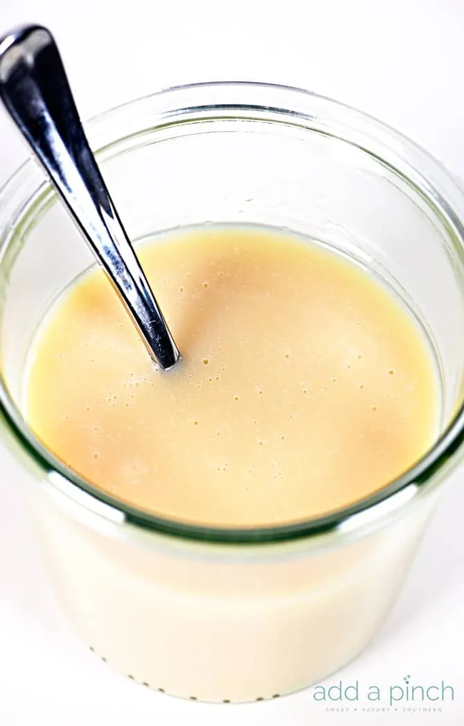 Homemade sweetened condensed milk in a glass jar with a spoon