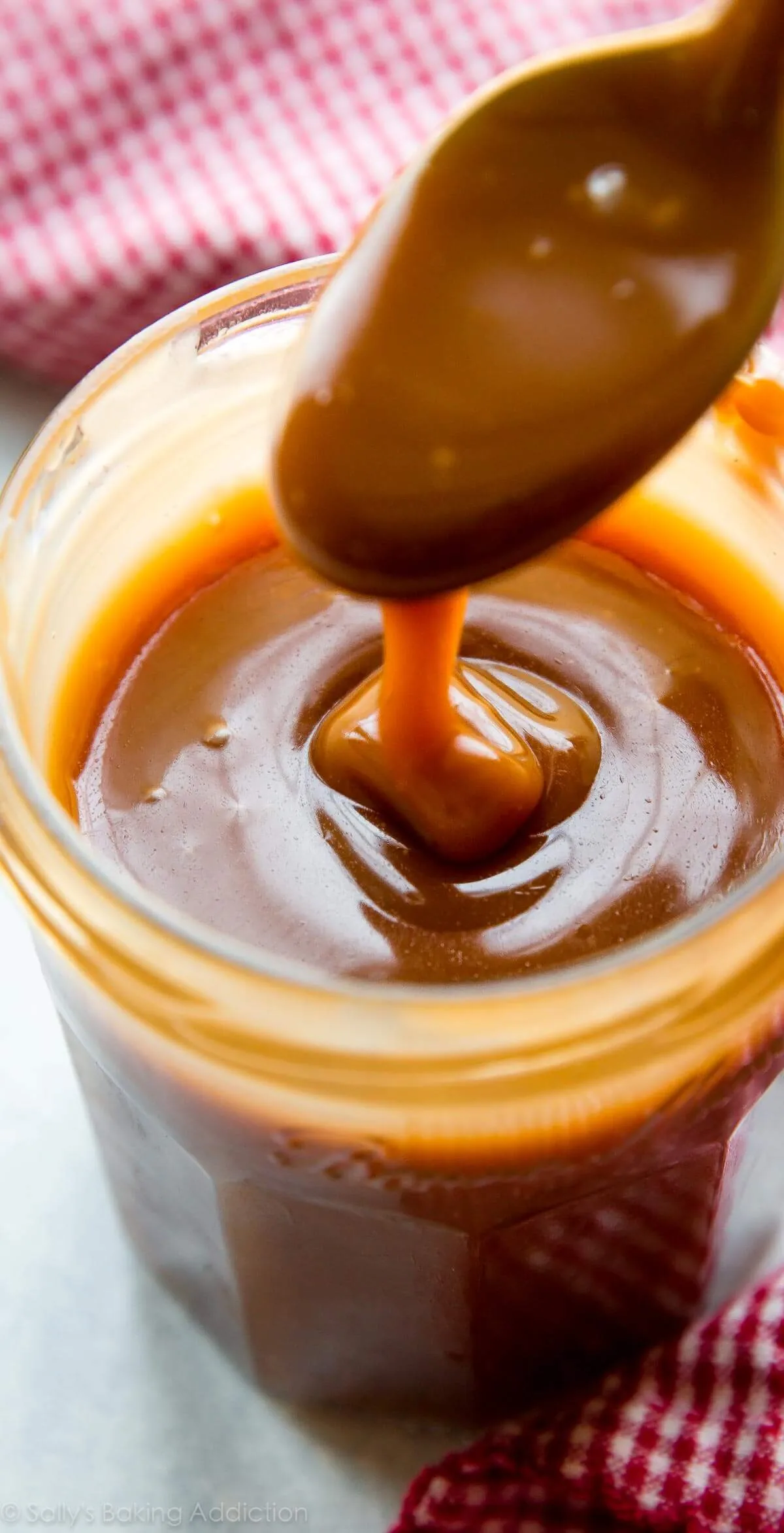 A spoon lifting glossy salted caramel out of a glass jar