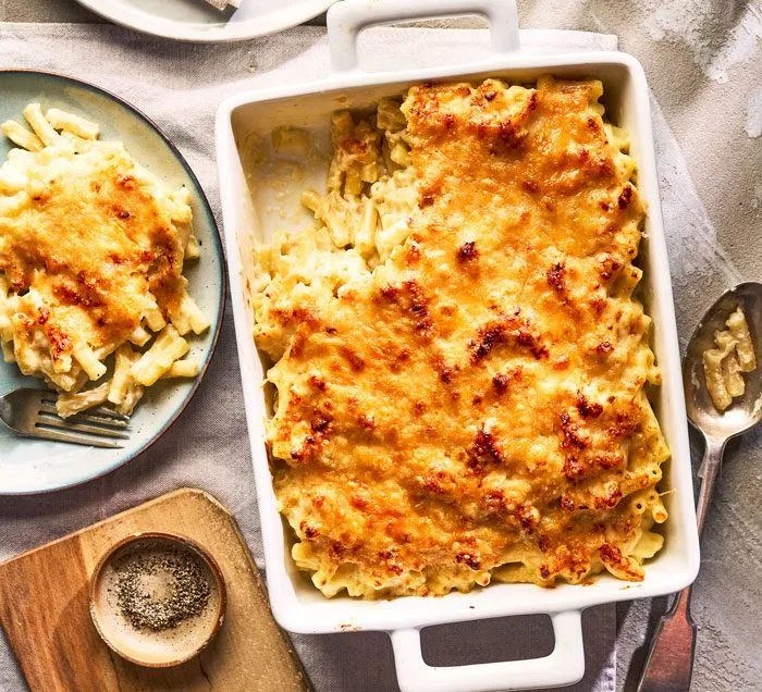 Baked macaroni cheese with a golden, crisp top in a white dish, with a portion served on a plate