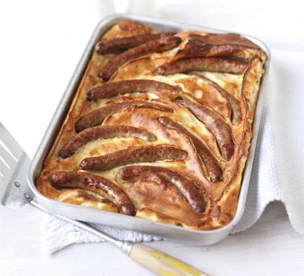 Toad in the hole in a metal roasting tin, with browned chipolatas set in puffed golden batter