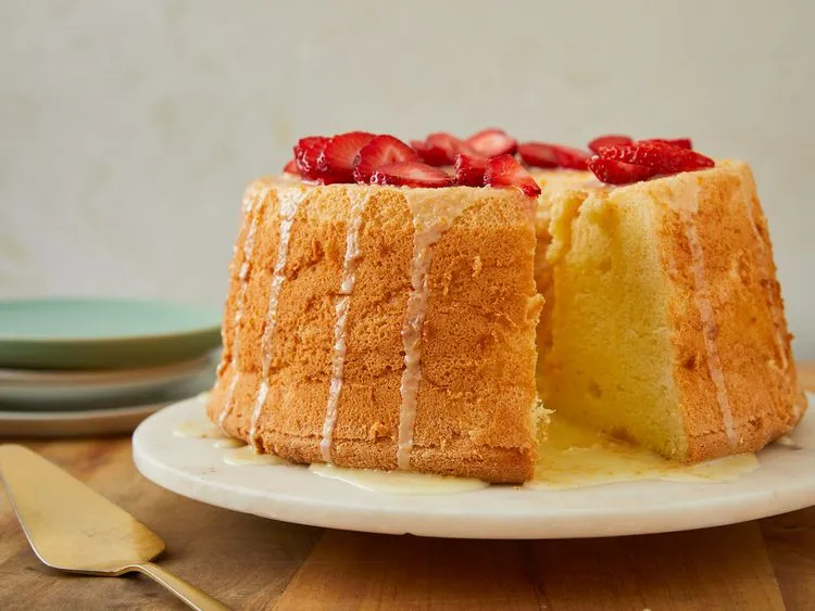 Chiffon cake on a marble stand, drizzled with glaze and topped with sliced strawberries, with a wedge cut out